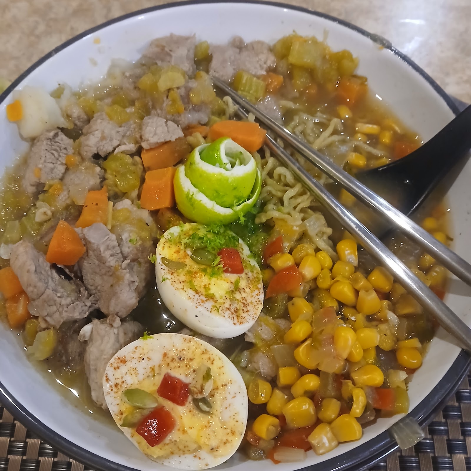 Close-up of ramen bowl with pork, carrots, corn and a lime rose garnish